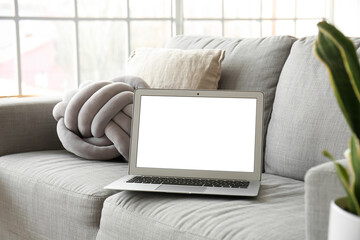 Modern laptop on sofa in light room