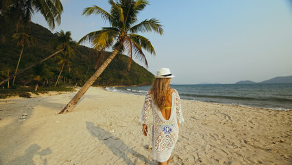 Back View of Sexy Woman in a White Tunic on the Beach, near the Sea. Happy Hot Blonde with Wet Curly Hair. Lady Tourist Enjoying Vacation Time, Walks has Fun. Concept of Rest at Resort Coastline