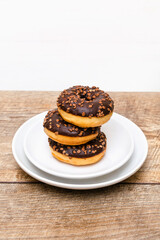 Mini donuts covered with chocolate glaze. Stack of tasty sweet sugar creamy or icing doughnuts dessert food on plate on kitchen. national donuts day