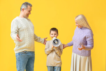 Little boy with megaphone and his grandparents in warm sweaters on yellow background
