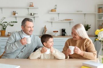 Little boy and his grandparents in warm sweaters with cups of cocoa at home