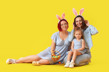 Happy lesbian couple with little daughter and Easter eggs on color background