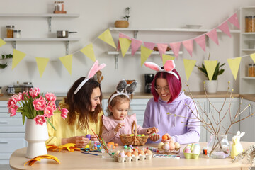 Young lesbian couple with little daughter during painting of Easter eggs in kitchen