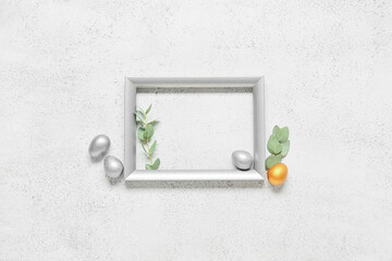 Composition with photo frame, painted Easter eggs and eucalyptus branches on light background