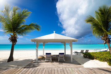 A tropical paradise beach with palm trees, a gazebo, sun chairs and turquoise sea without people
