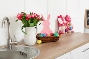 Basket with Easter eggs and tulips in vase on counter near light wall