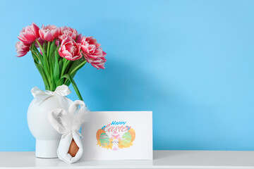Greeting card with text HAPPY EASTER, egg and tulips in vase on table near blue wall
