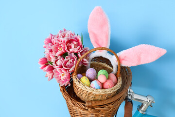 Bicycle with baskets, tulips, Easter eggs and bunny ears near blue wall