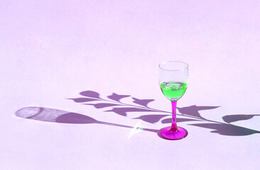 Minimal concept a glass of wine with green drink. Shadows of glass and leaves on pastel lavender backgraound