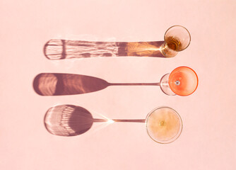 Creative concept a glasses of wine and shampagne on sunny day. Minimal idea of shadows on pastel pink background. Flat lay. © Suzana