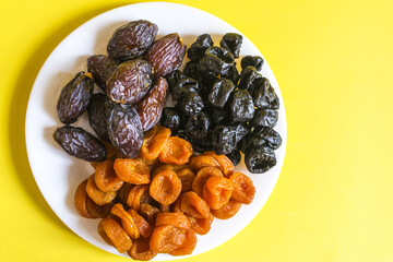Dried apricots, prunes and dates dried fruits on a light plate close-up.	