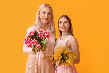 Young woman with her mother and flowers on yellow background