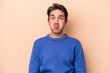 Fototapeta premium Young caucasian man isolated on beige background blows cheeks, has tired expression. Facial expression concept.