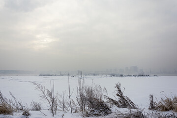 High-rise buildings in an industrial haze against the background of a frozen river.