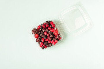 A mixture of frozen strawberries, cranberries, currants, blueberries in close-up in a transparent bowl on a light background.
