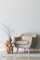 Tree branches with colorful Easter eggs on table and armchair near light wall © Pixel-Shot