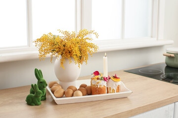 Tray with Easter cakes, eggs and vase with mimosa flowers on kitchen counter