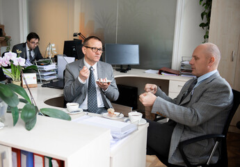 Colleagues having a coffee break in the office at their work desk
