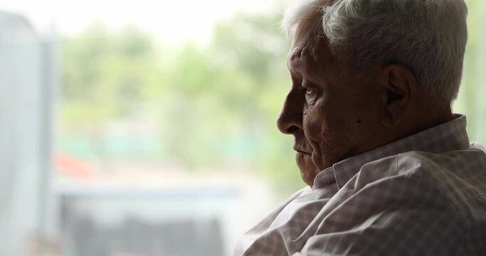 Close up face of older man sits on couch lost in sad thoughts, 80s grandfather suffers from loneliness at nursing home. Chronic senile diseases, dementia, life regrets, nostalgia, melancholy concept