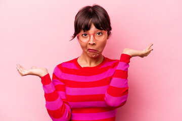 Young hispanic woman isolated on pink background doubting and shrugging shoulders in questioning...