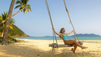 Woman spends her vacation at the seaside. The girl is swinging on a swing. Concept meditation, relaxation and walks, replenishment of energy and good happy mood.
