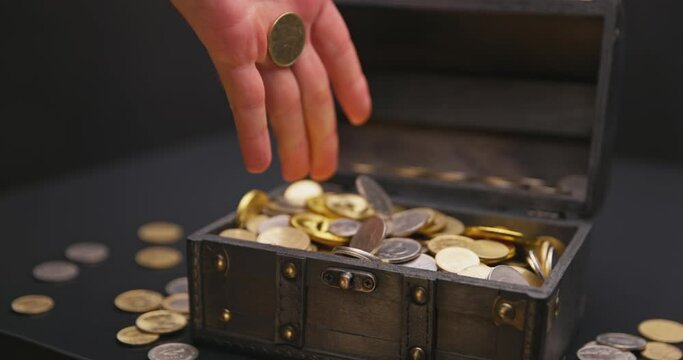 Hand putting coins into treasure chest slow motion footage
