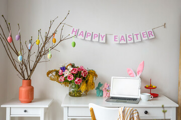 Workplace with modern laptop and stylish decor for Easter celebration near white wall