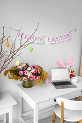 Workplace with modern laptop and stylish decor for Easter celebration near white wall