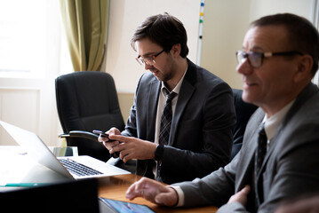 Young businessman using phone during roundtable business meeting