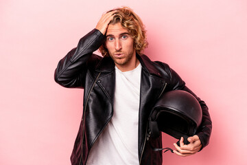 Young caucasian man with a motorcycle helmet isolated on pink background being shocked, she has...
