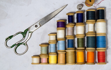 Multicolored, vintage threads on wooden bobbins on a gray background and tailor's accessories scissors with a thimble from the good old days. Top view, copy space.