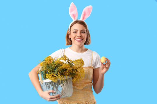 Beautiful Young Woman With Bunny Ears, Basket Of Flowers And Easter Egg On Blue Background
