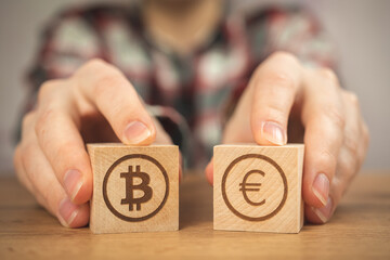 Bitcoin and euro symbol on wooden cubes in hands. Concept of cryptocurrency and cash background, wooden table