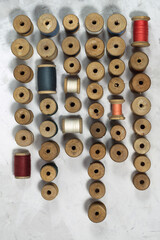 The threads on the wooden bobbin are arranged in a pattern on a gray background. Vintage sewing threads for needlework.Top view, flat lay.