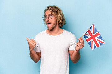 Young student caucasian man holding an United Kingdom flag isolated on blue background points with...