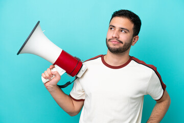 Young Brazilian man isolated on blue background holding a megaphone and thinking
