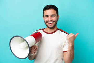 Young Brazilian man isolated on blue background shouting through a megaphone and pointing side