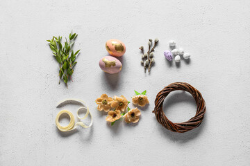 Composition with Easter eggs, wreath, flowers, green branches and ribbon on light background