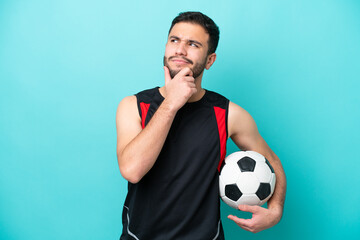 Young football player Brazilian man isolated on blue background having doubts