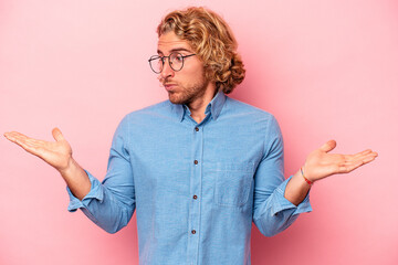 Young caucasian man isolated on pink background confused and doubtful shrugging shoulders to hold a...