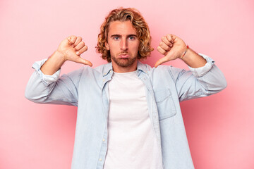 Young caucasian man isolated on pink background showing a dislike gesture, thumbs down....