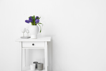 Vase with flowers and stylish decor on standing desk near white wall