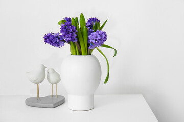 Vase with flowers and decor on table near light wall