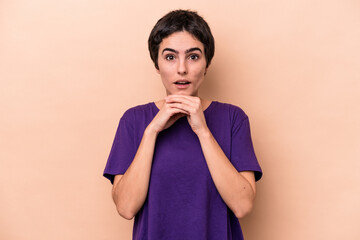 Young caucasian woman isolated on beige background praying for luck, amazed and opening mouth looking to front.