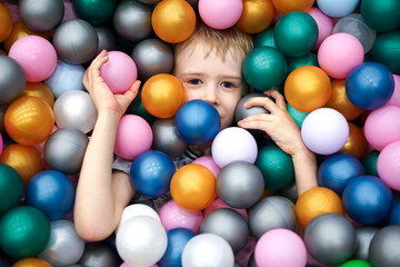 Fototapeta na wymiar Smiling child in the play pool with plastic balls. Boy in the children's entertainment center