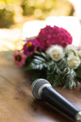 Microphone on a wooden table next to wedding bouquet with carnation flowers