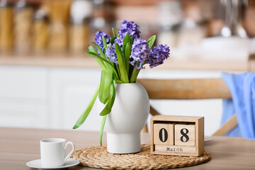 Cube calendar with date 8 MARCH, flowers and cup of coffee on dining table. International Women's Day celebration