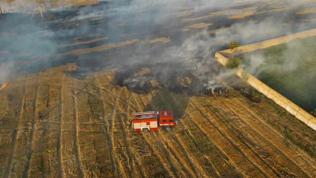 Massive fire in on field near village. Burning large areas of dry stubble at same time. Fireman bravely extinguishes flame with water. Emergency case for danger mission and rescue nature saving