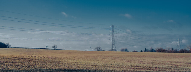 Electricity pylons in British countryside with wind turbines in the distance