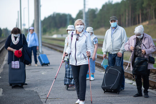 A group of senior friends in face masks on the platform waiting for a train